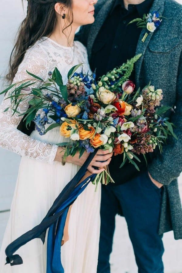 Bride and groom holding colorful flower bouquets against a light background