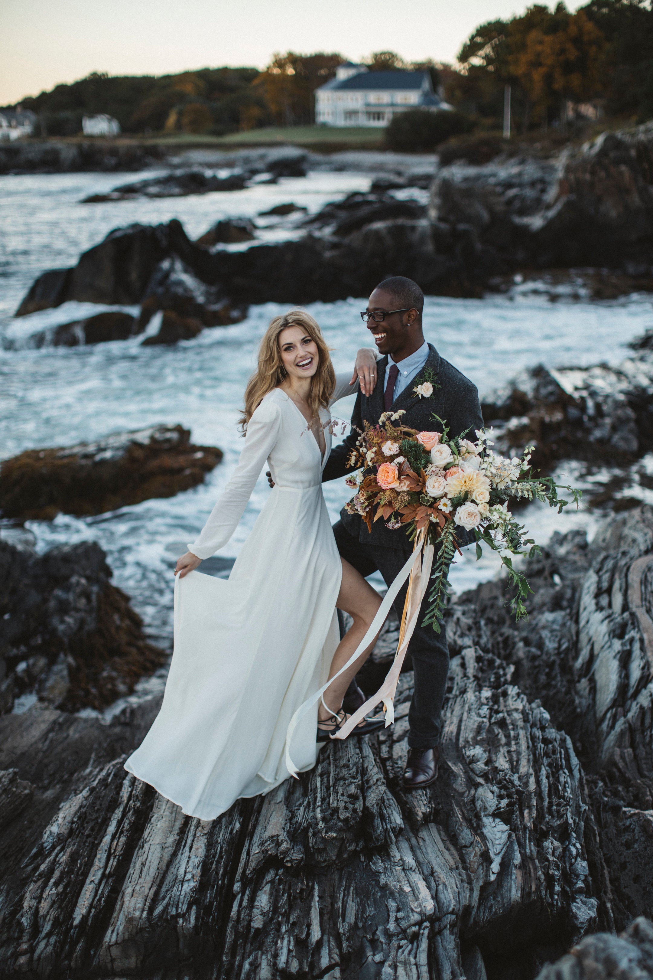 Couple standing on rocky coastal landscape with a house in the background