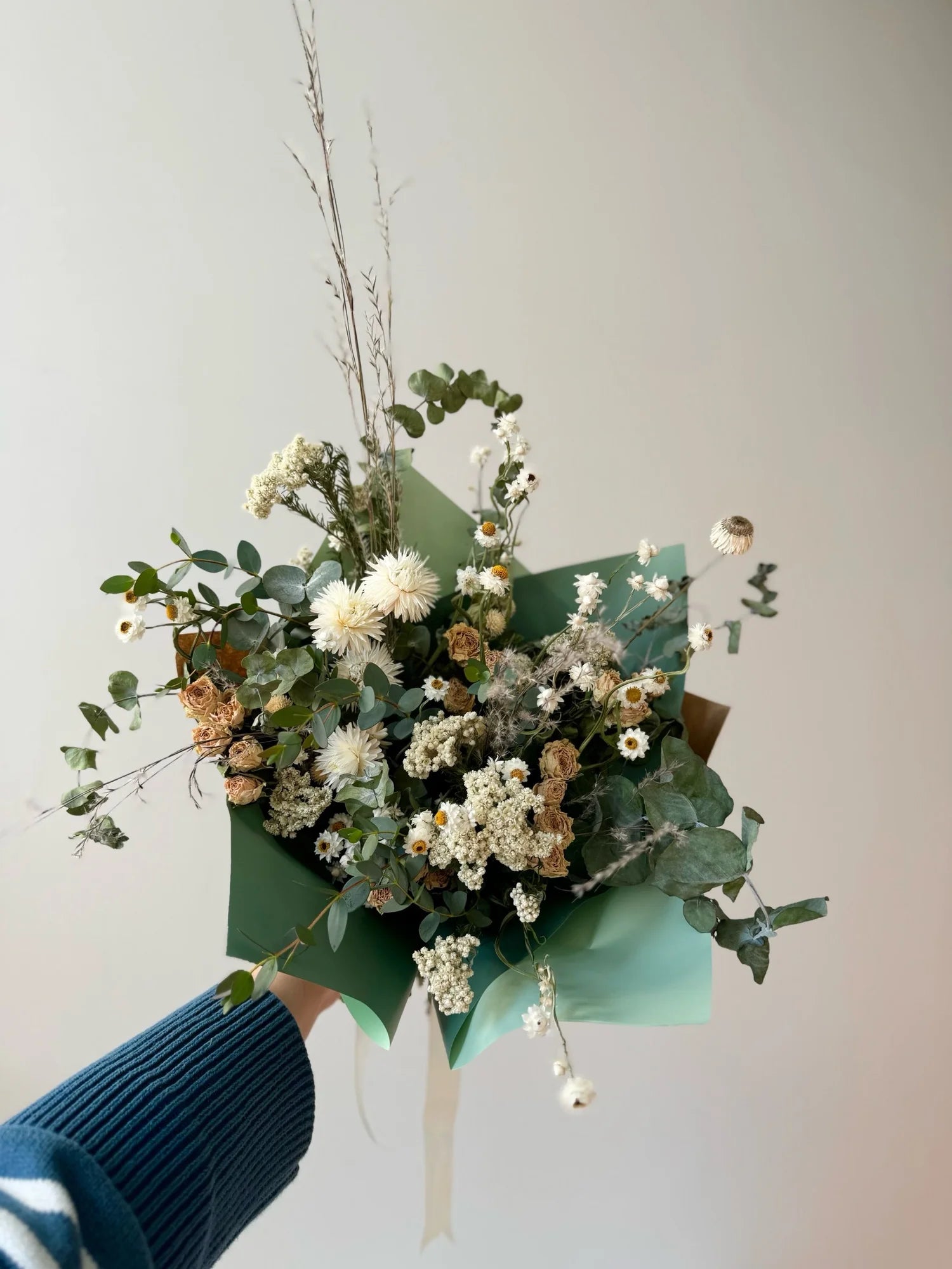 Bouquet of flowers with green paper wrap held by a person wearing a blue sweater.
