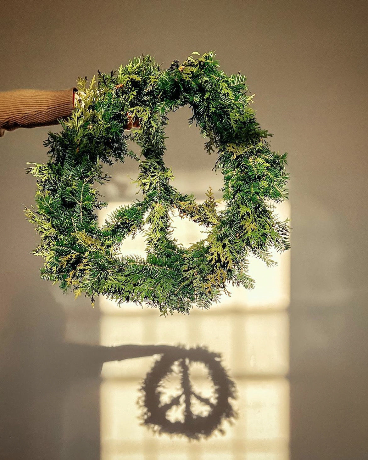 Green peace shaped wreath on a plain wall with a soft shadow
