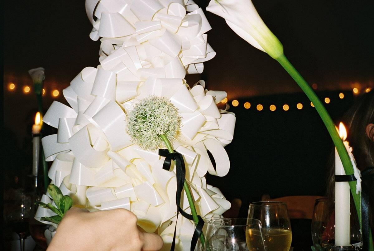 Decorative arrangement of white flowers and ribbons with a candle in the background.
