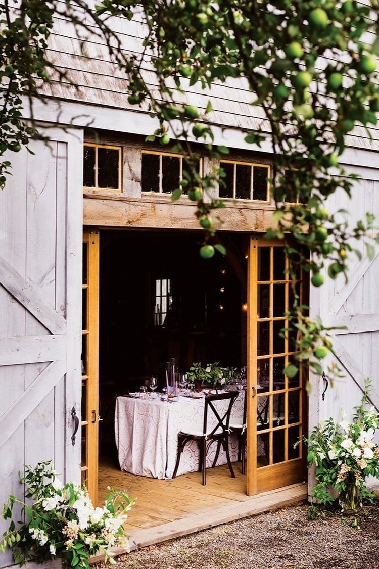 Barn door open to reveal a dining setup inside, surrounded by greenery.