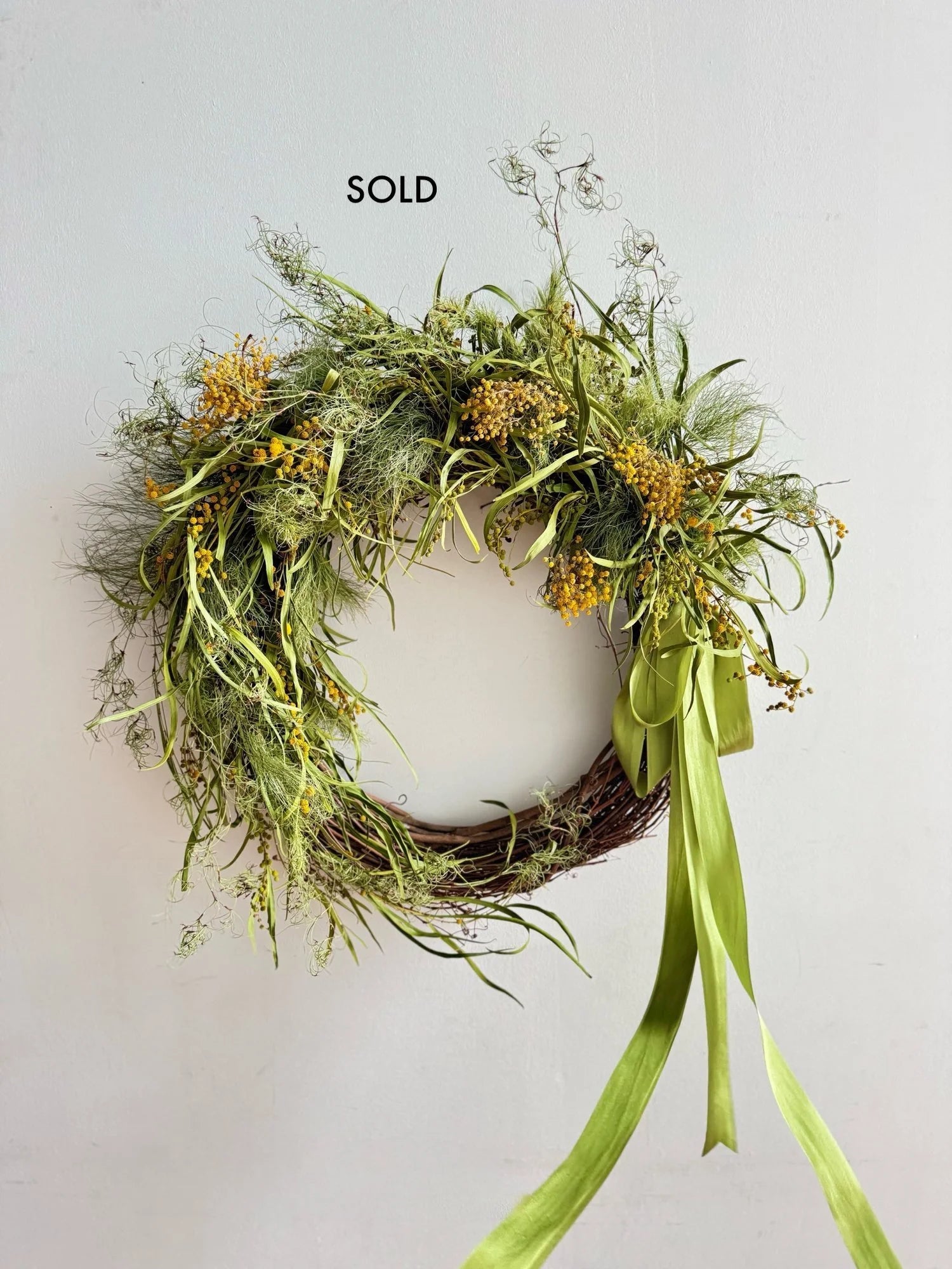 Wreath with greenery and a green ribbon on a light gray background