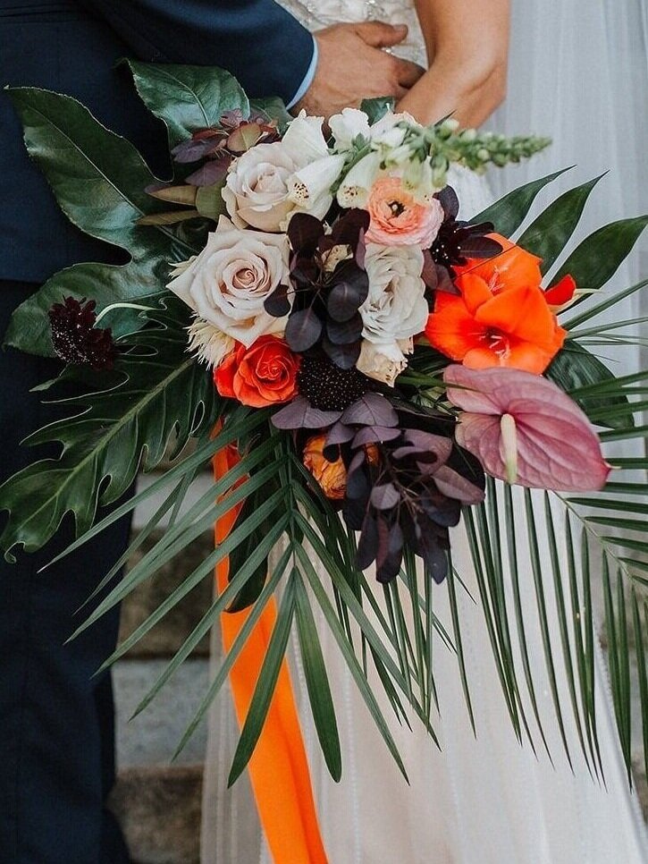Bouquet of flowers held by a person, with a focus on the vibrant colors and greenery.