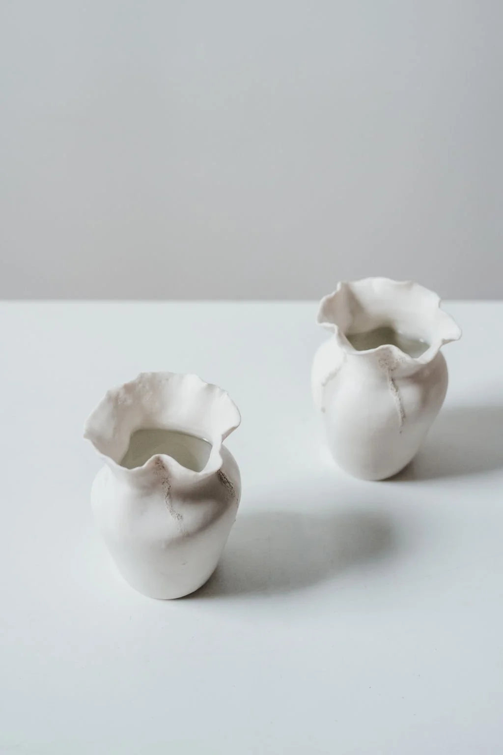 Two white ceramic vases on a light gray surface with a plain background