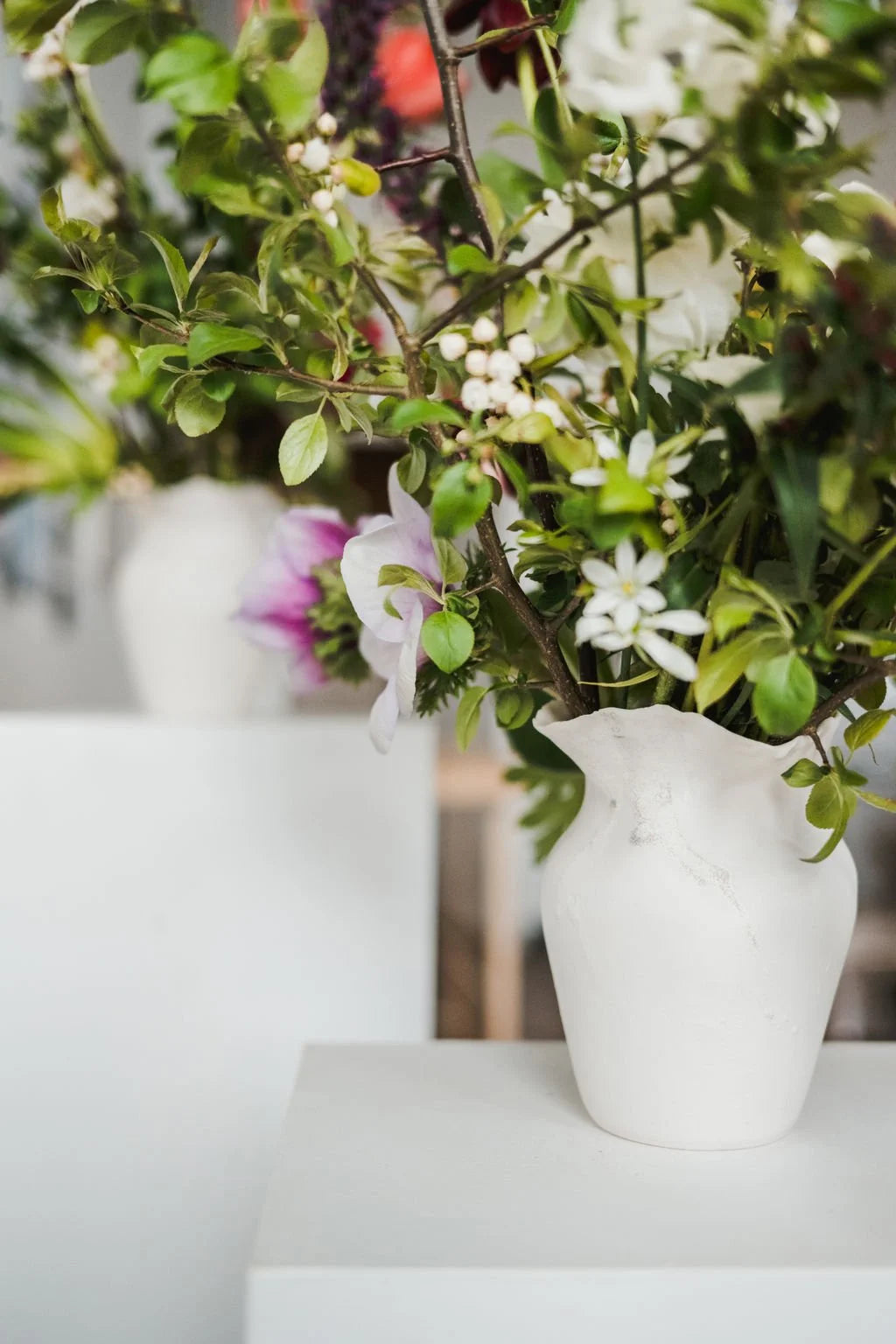 White vase with greenery and flowers on a white surface