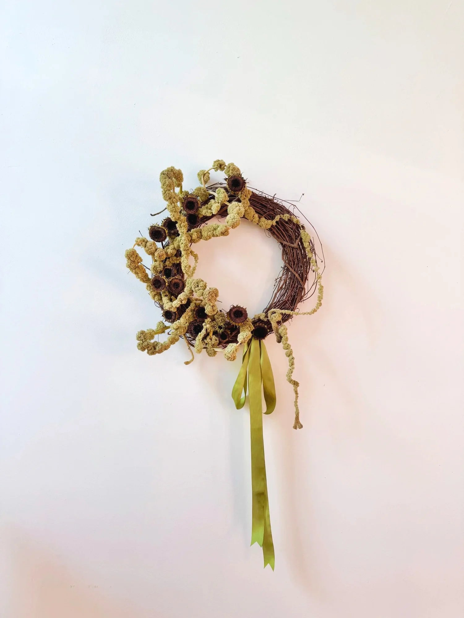Decorative headpiece with dried flowers and green ribbon on a white background