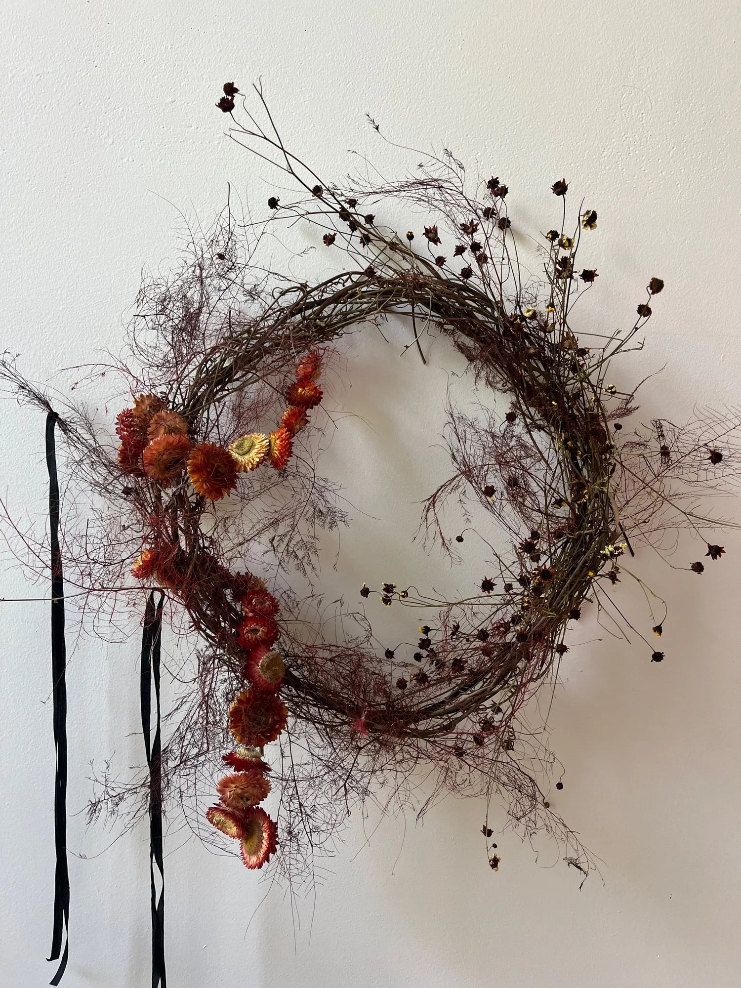 Decorative wreath with dried flowers and branches on a white wall