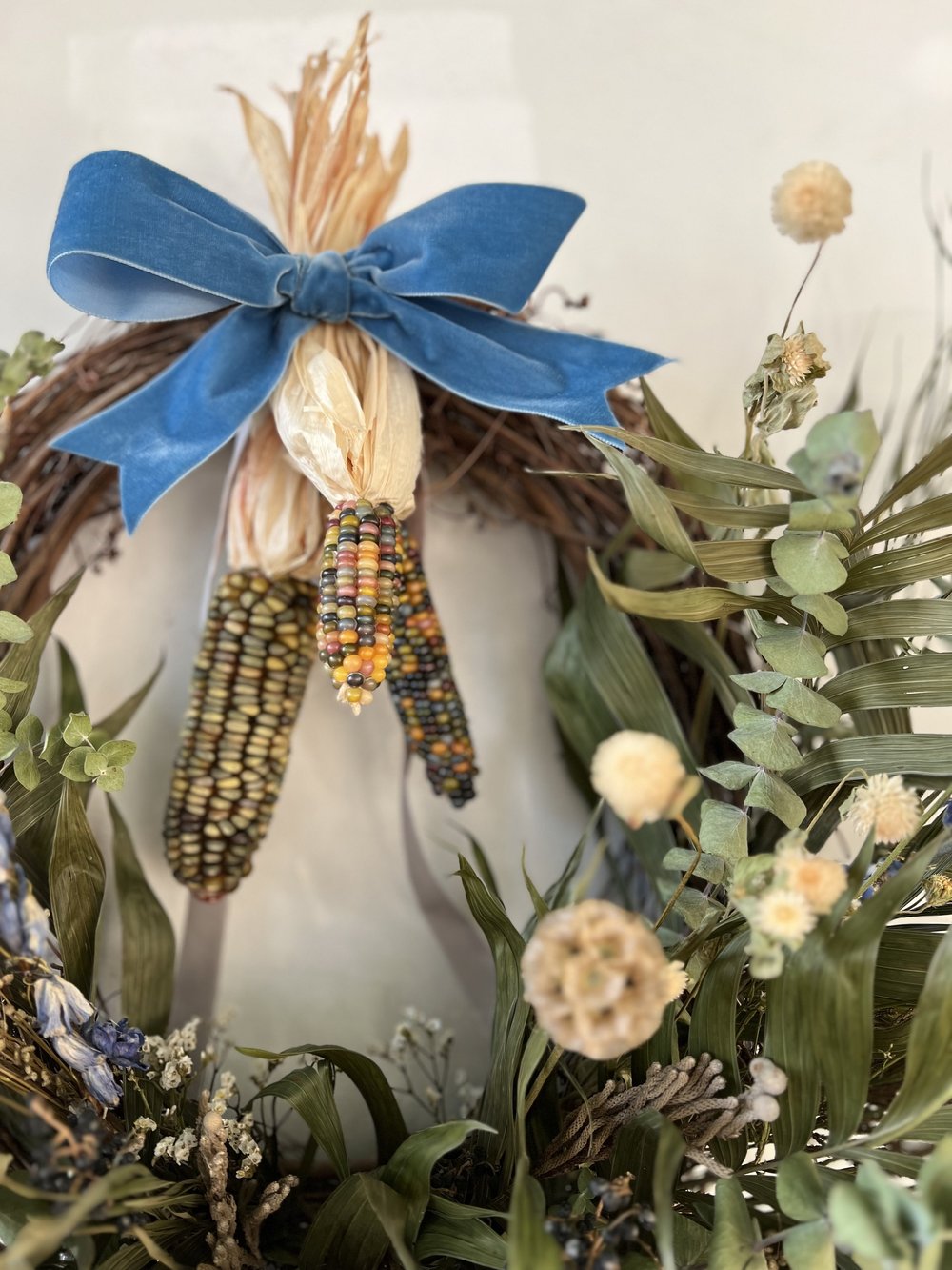 Decorative wreath with corn, blue ribbon, and greenery on a white background