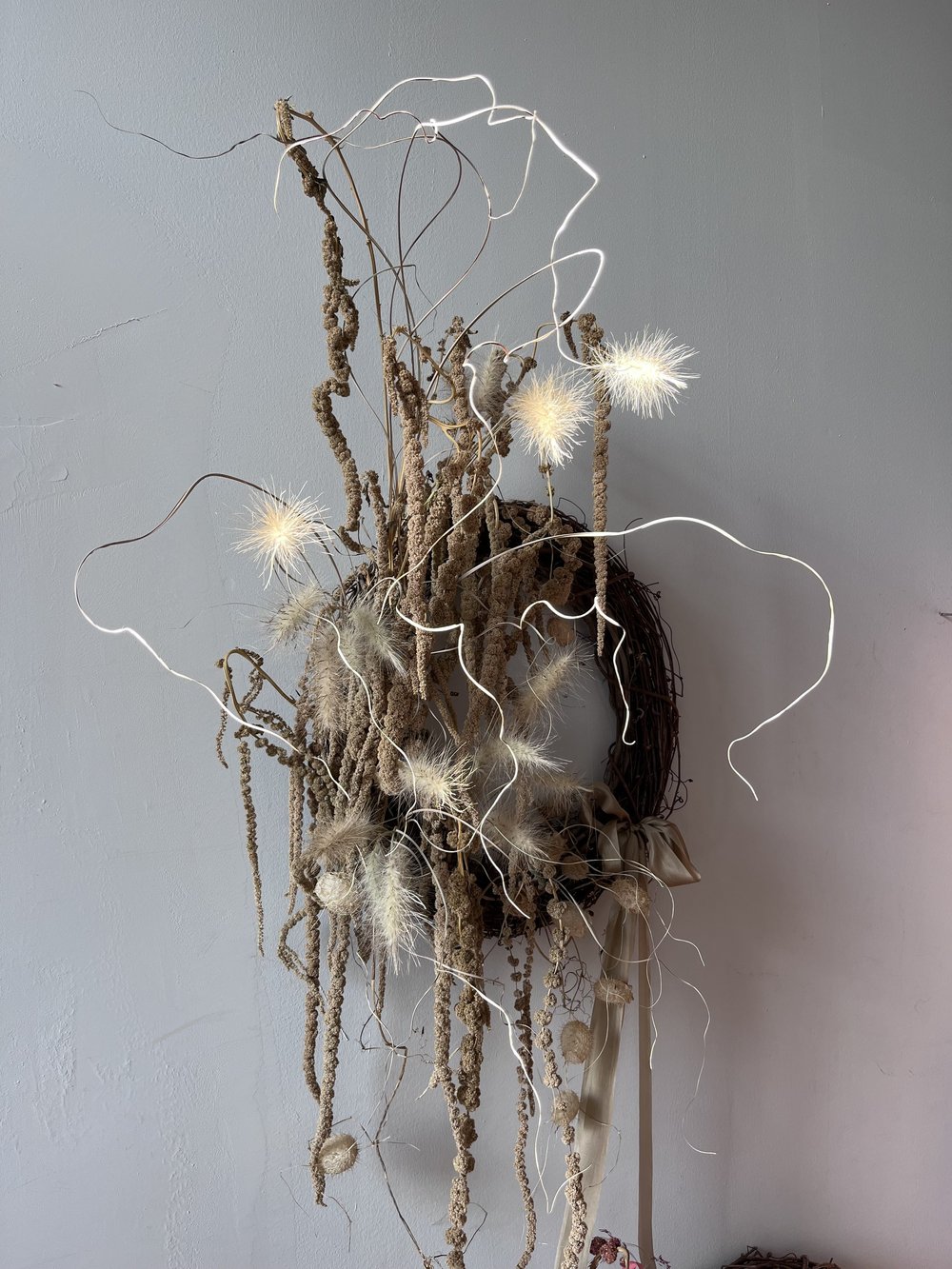Decorative wall piece with string lights and natural elements against a plain wall.