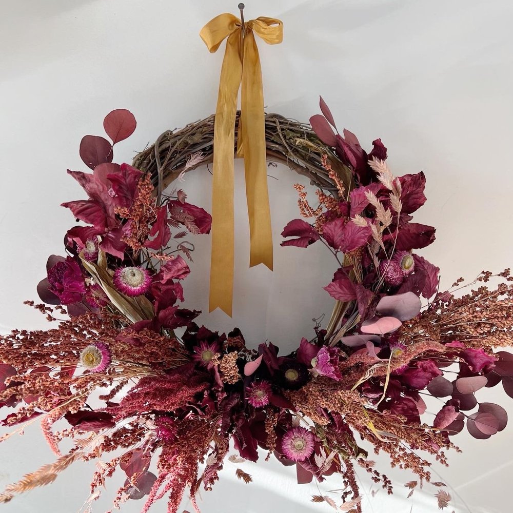 Decorative wreath with pink flowers and a yellow ribbon on a white background