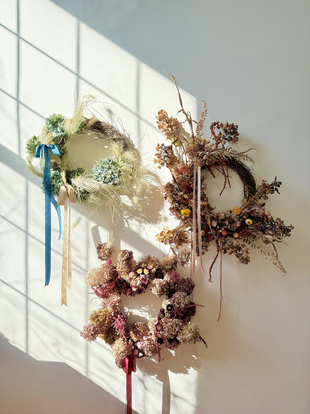Three decorative wreaths on a white wall with sunlight casting shadows.
