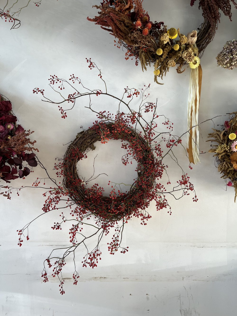 Decorative wreaths with berries and flowers on a white wall