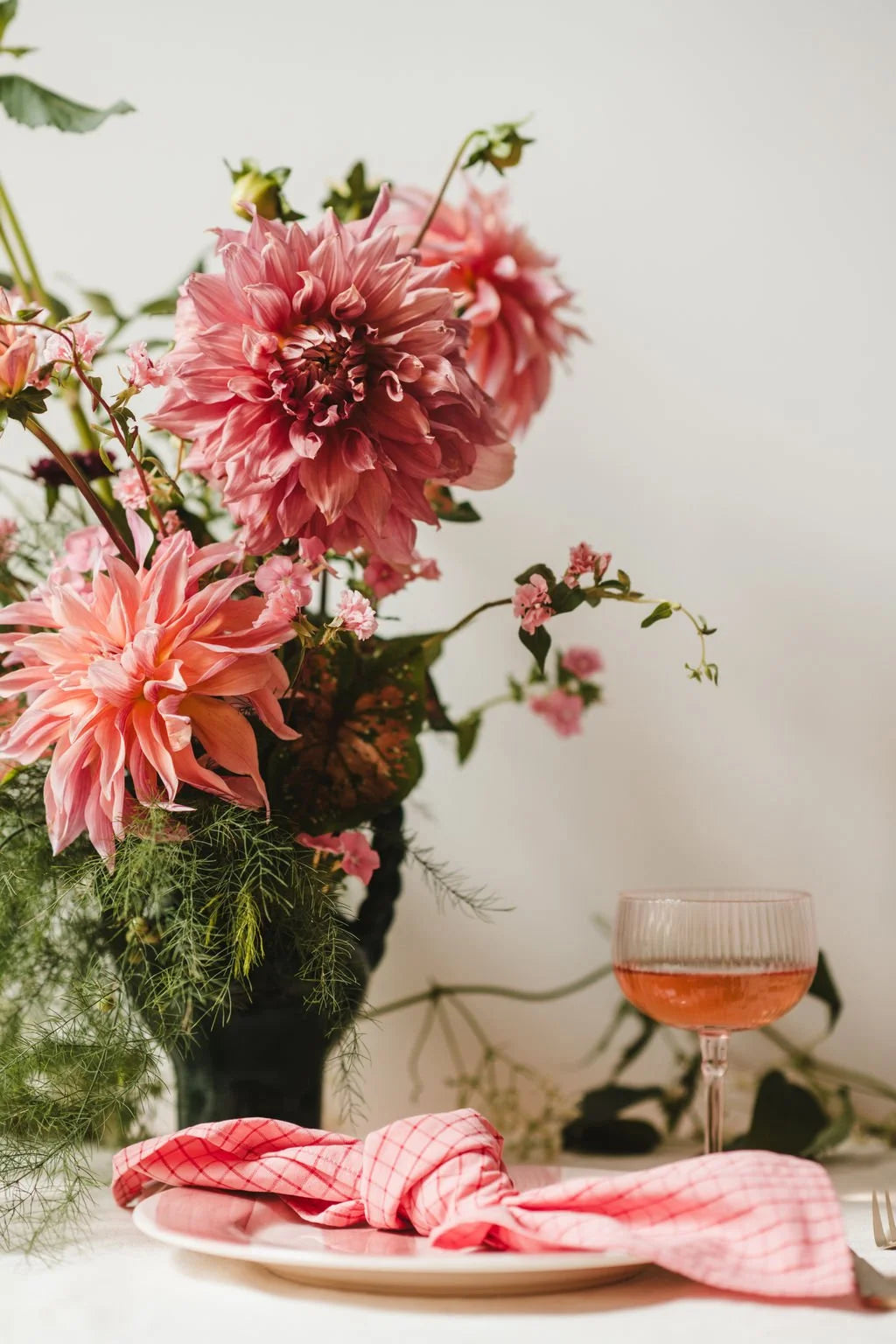 Pink floral arrangement with a glass of pink drink on a table.