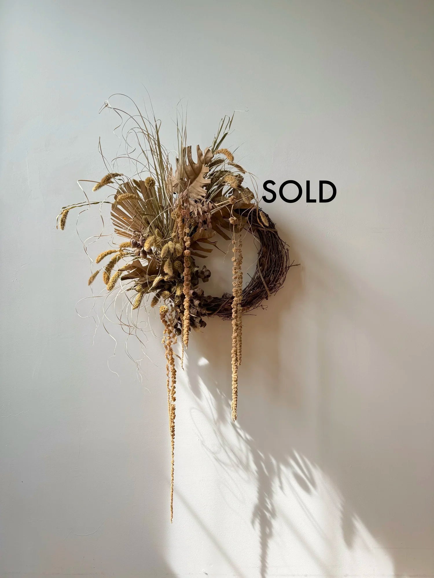 Decorative wreath with air plants on a white wall, labeled 'SOLD'.