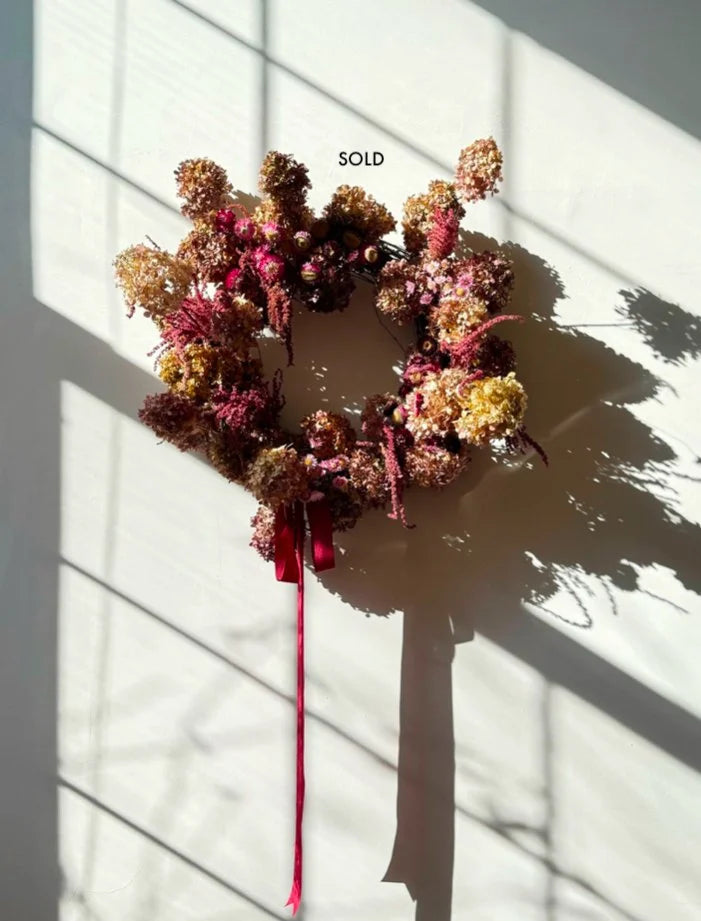 Dried flower wreath with a pink ribbon on a white wall