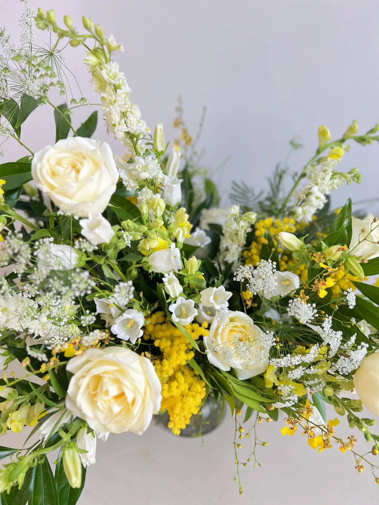 Bouquet of white and yellow flowers with greenery on a light gray background