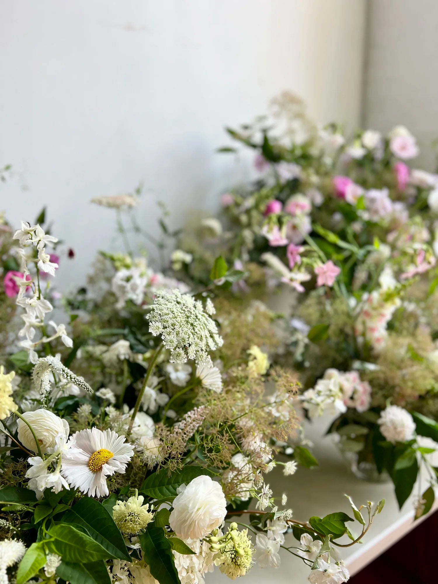 Close-up of a floral arrangement with white, pink, and green flowers on a white background.