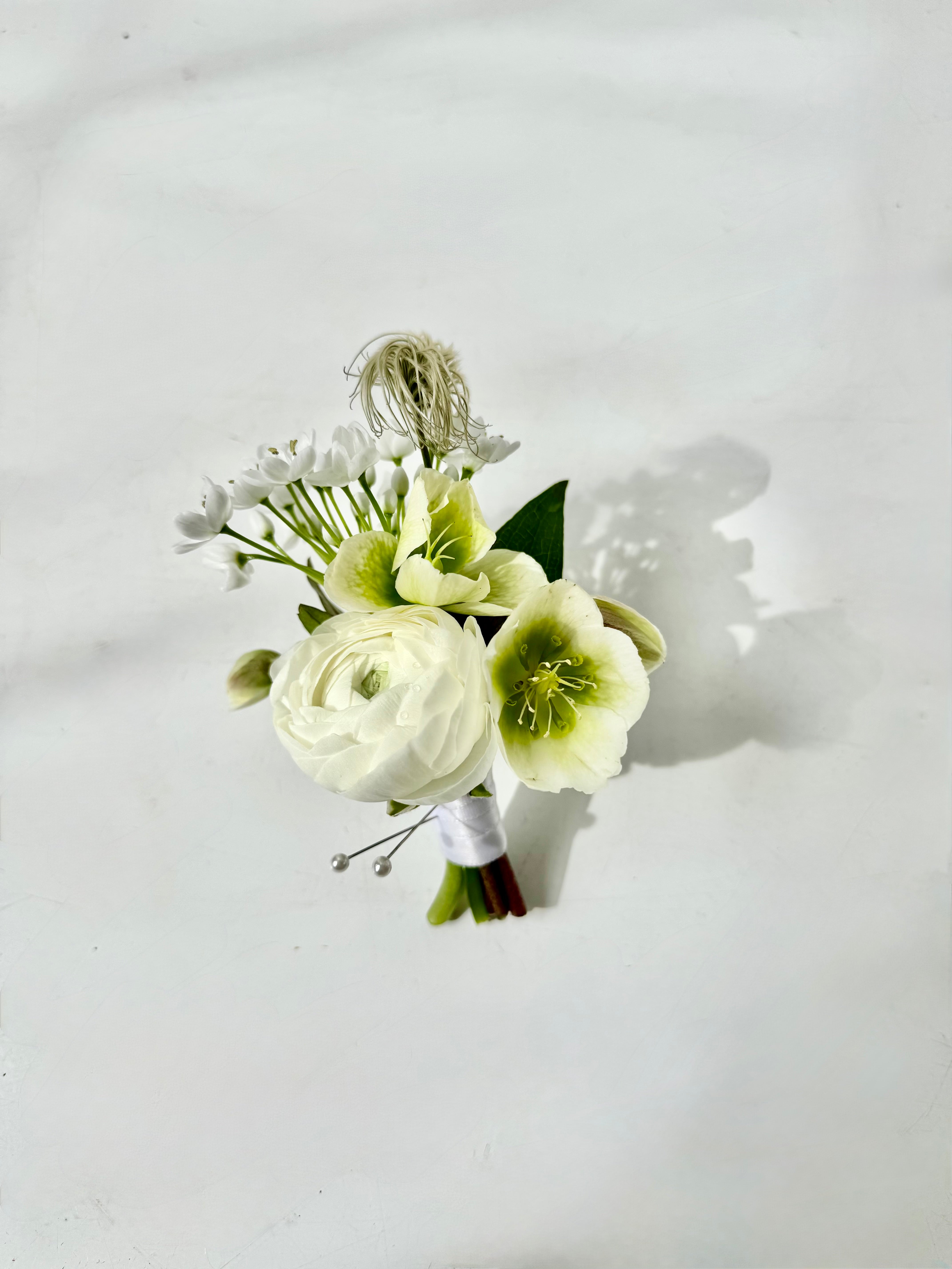 garden style boutonniere with white and green flowers featuring ranunculus, allium, and hellebore for wedding orders in southern maine