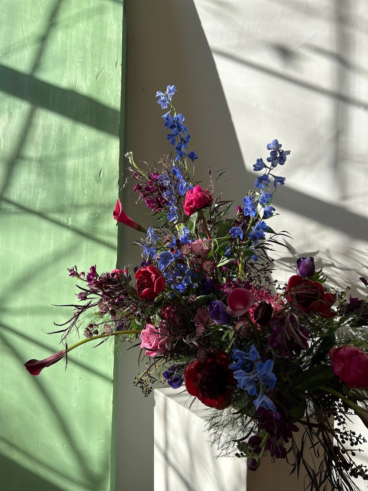 Bouquet of flowers with red, pink, and blue colors on a white surface with shadows.