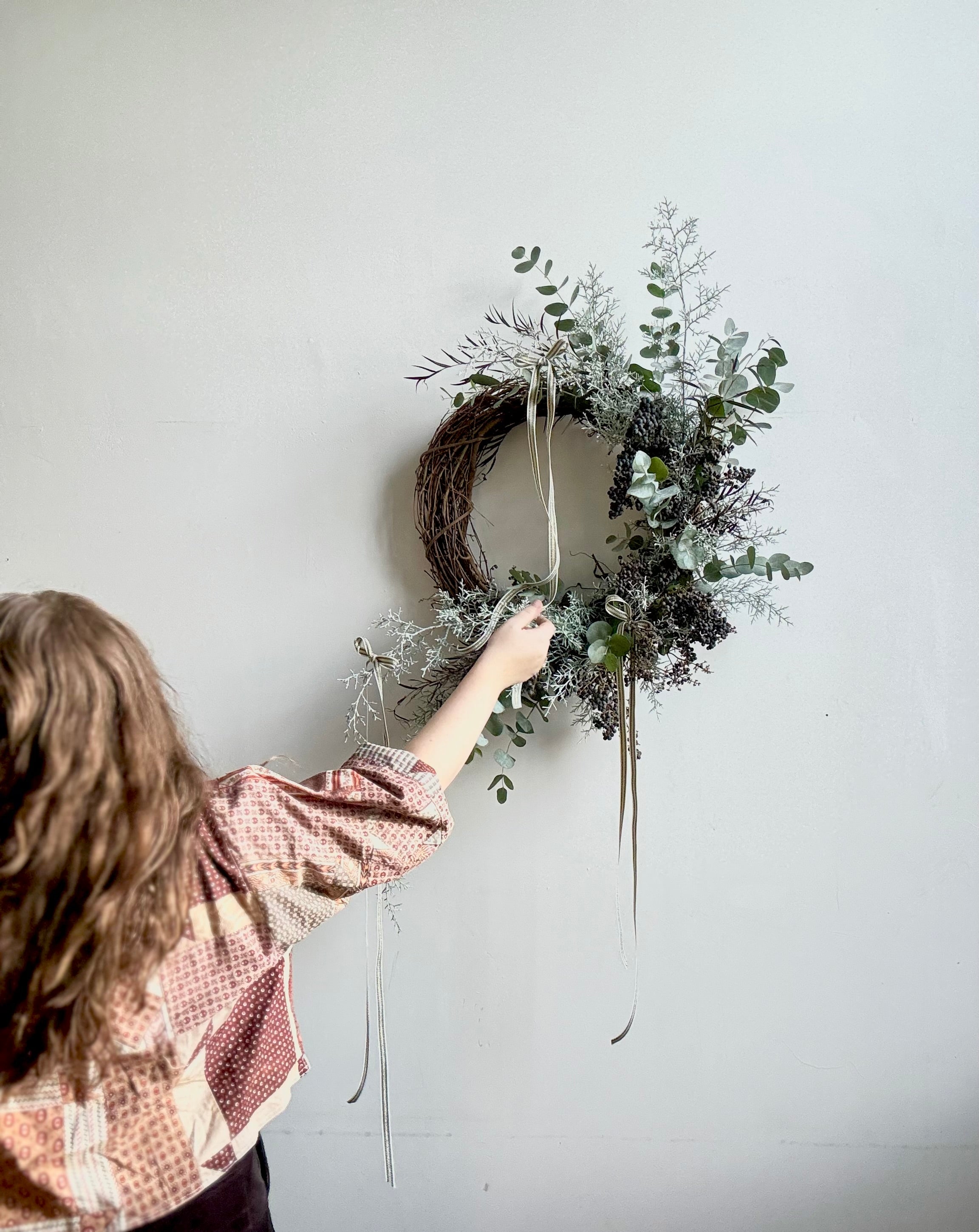 Maine florist arranging an evergreen holiday wreath with a white background.
