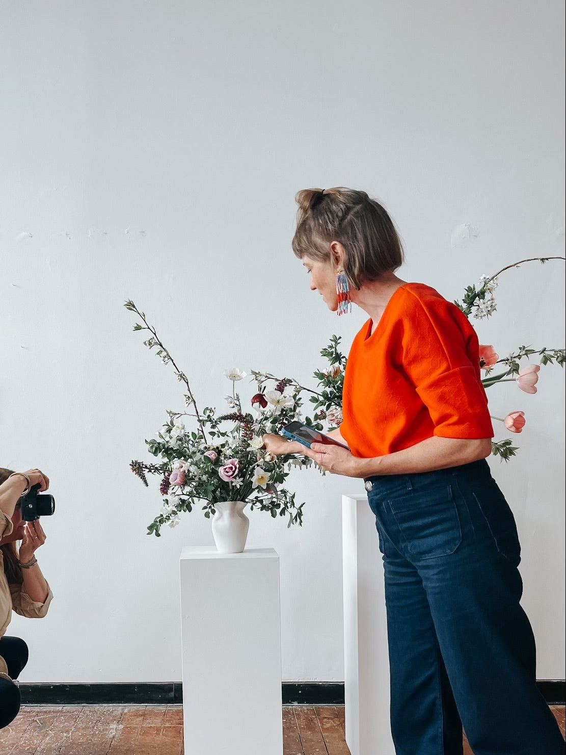 Photographer taking a photo of a florist touching up a floral arrangement in a room.