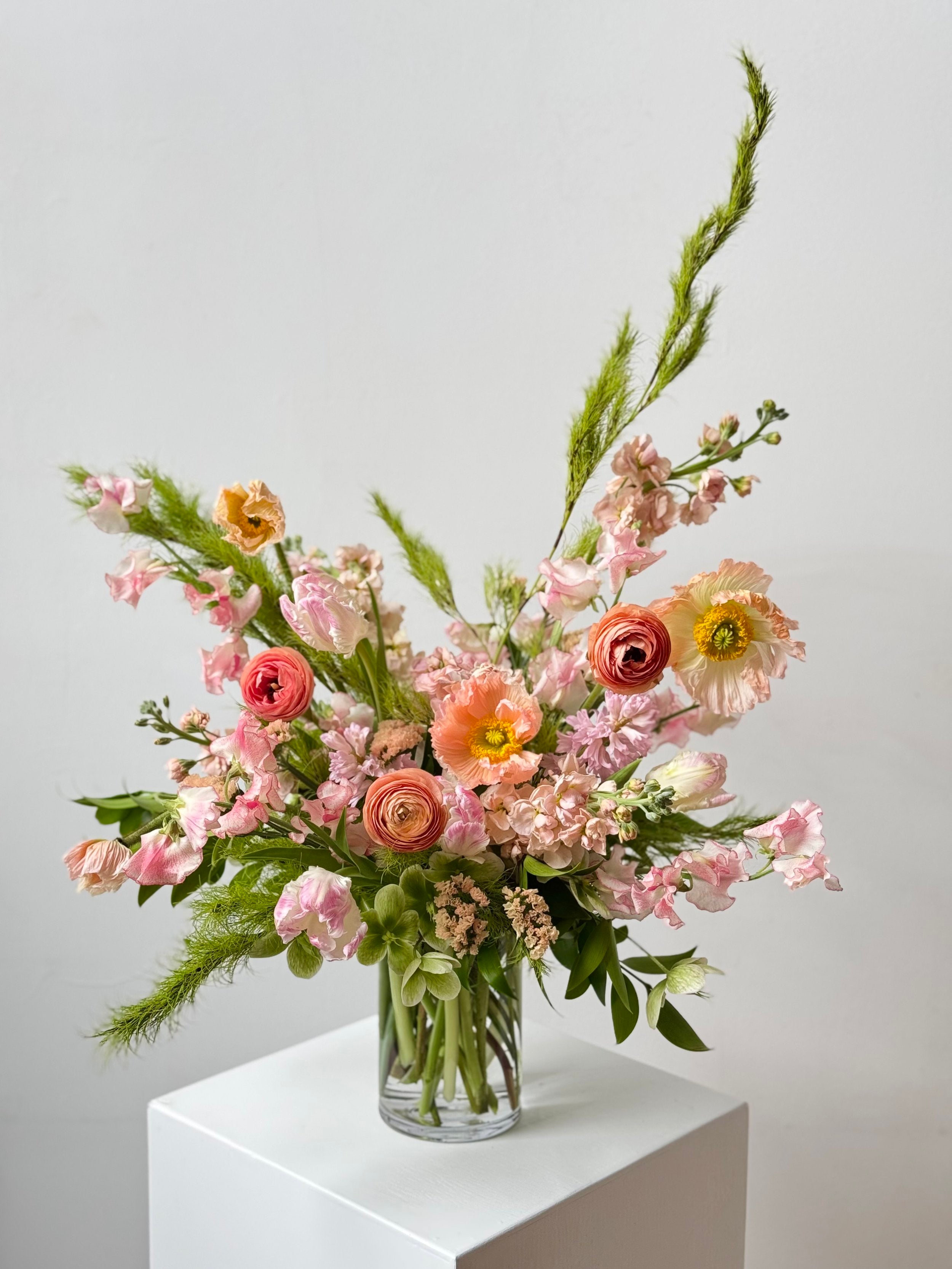 Bouquet of flowers in a clear vase on a white surface with a light gray background
