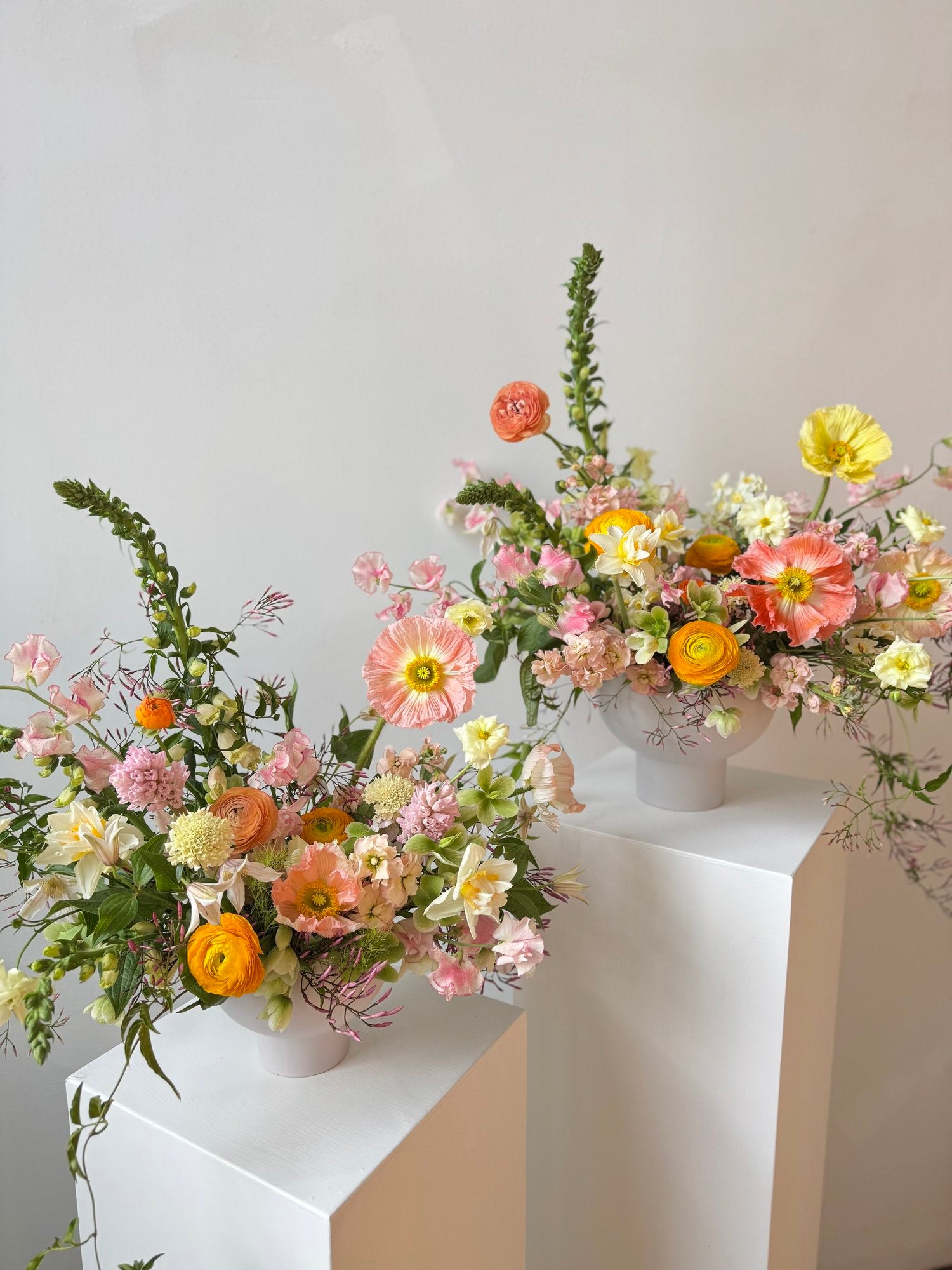 Two floral arrangements on white pedestals against a light gray background