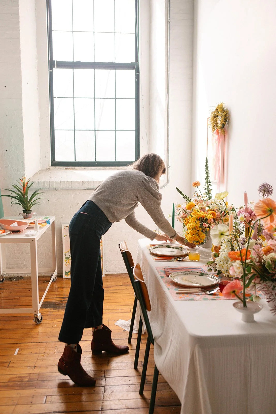 Person setting a table with floral arrangements in a bright room.