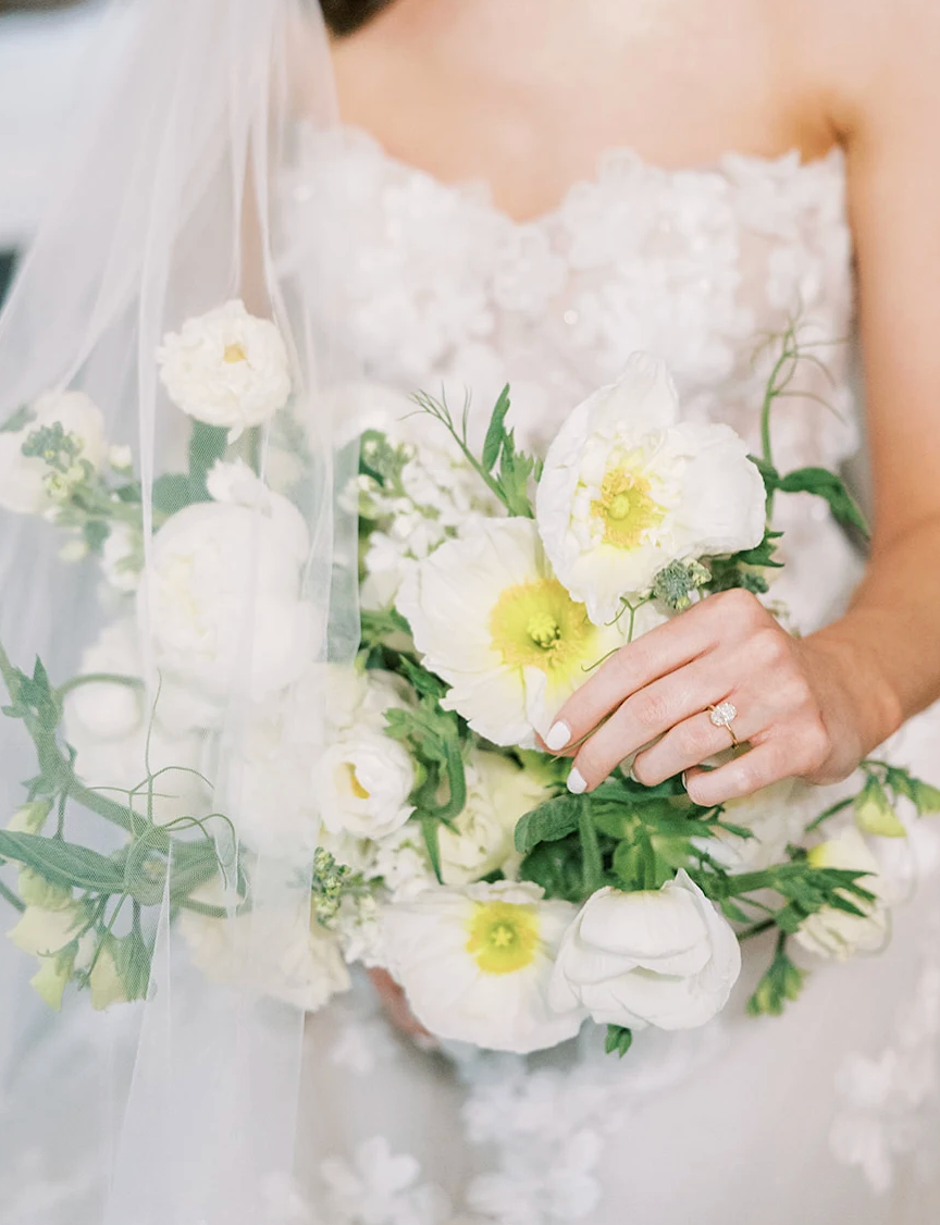 Bride holding a bouquet of white and yellow flowers with a blurred background