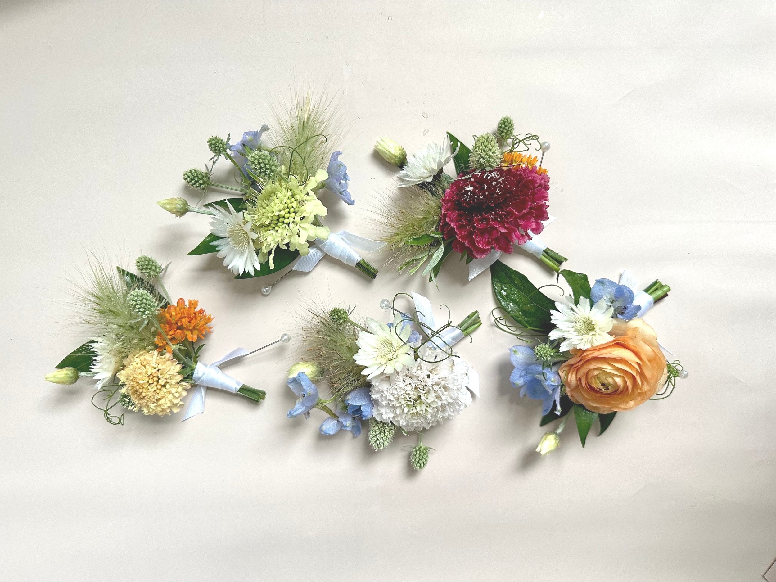 Four floral boutonnieres arranged in a circular pattern on a light background