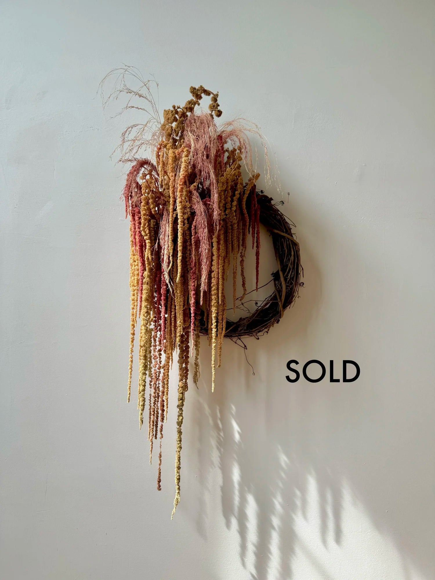 Decorative wreath with hanging strands on a white wall, labeled 'SOLD'.