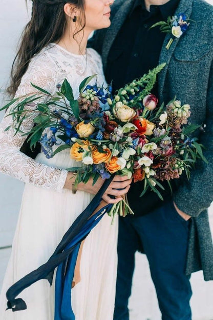 Bride and groom holding colorful flower bouquets against a light background