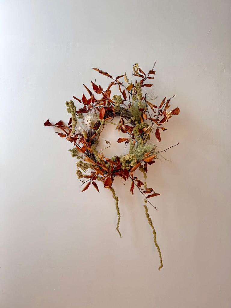 Wreath with autumn leaves and branches on a plain wall