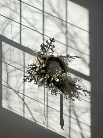 Decorative wreath with maine grown evergreens greenery against a window with sunlight filtering through