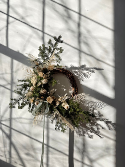 Decorative wreath with greenery and flowers against a light background