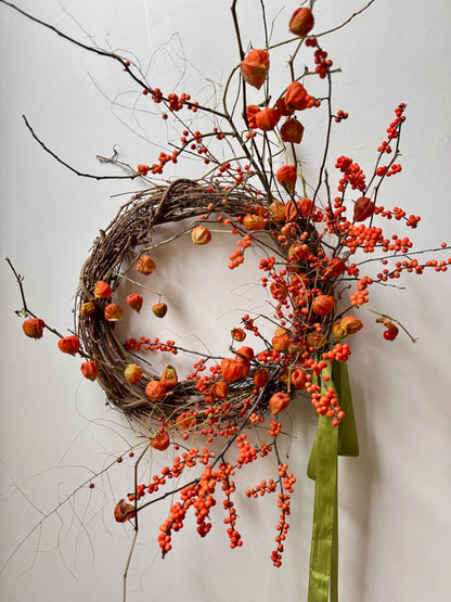 Decorative wreath with orange berries and green ribbon on a white background