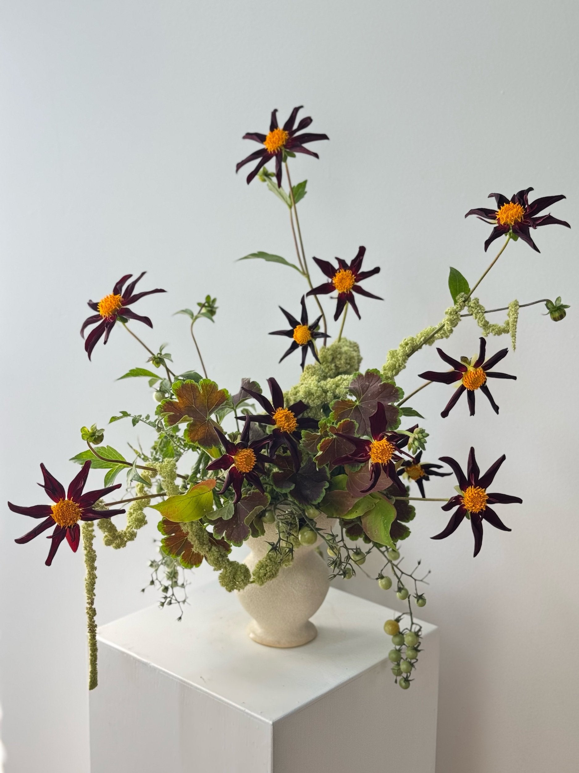 Floral arrangement with dark purple and orange flowers in a white vase on a light gray background