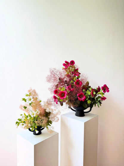 Two floral arrangements on white pedestals against a light background