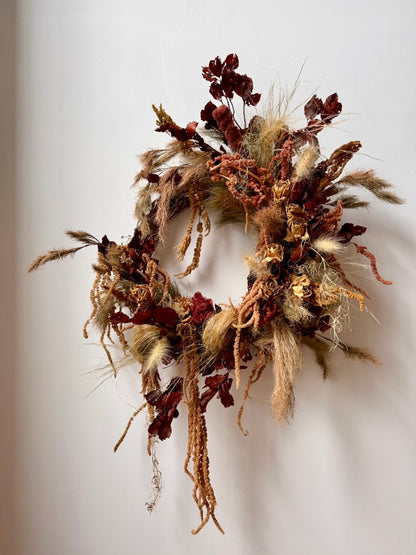 Decorative wreath with dried flowers and herbs on a white wall