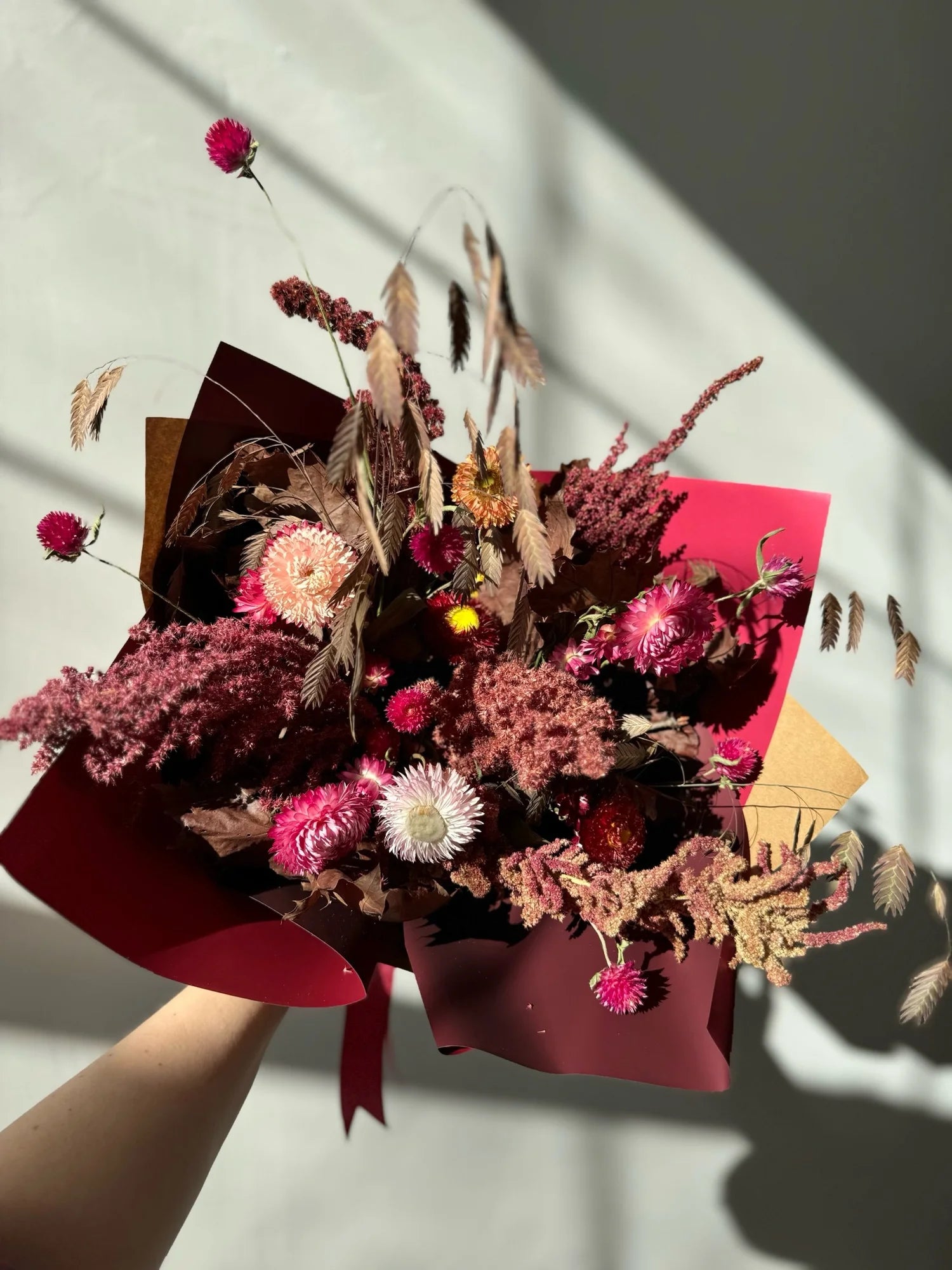 Bouquet of dried flowers wrapped in red paper held by a hand on a light background