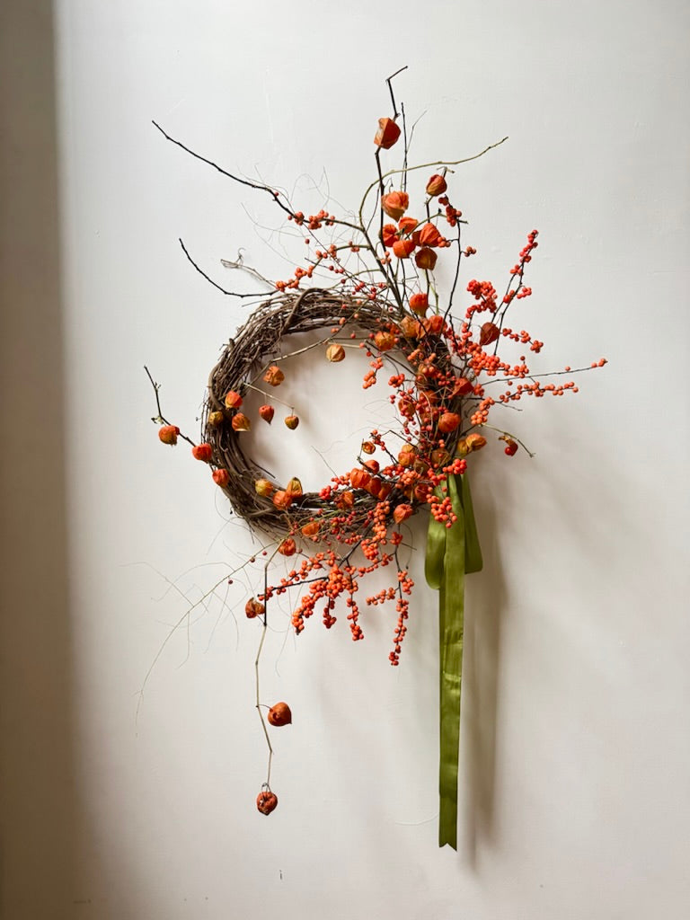 Decorative wreath with berries and a green ribbon on a white wall