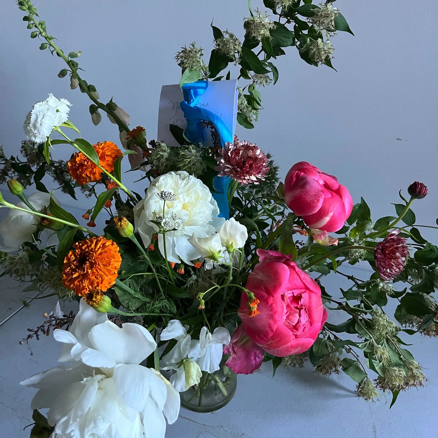 Bouquet of colorful flowers including pink, white, and orange blooms in a clear vase on a light background.