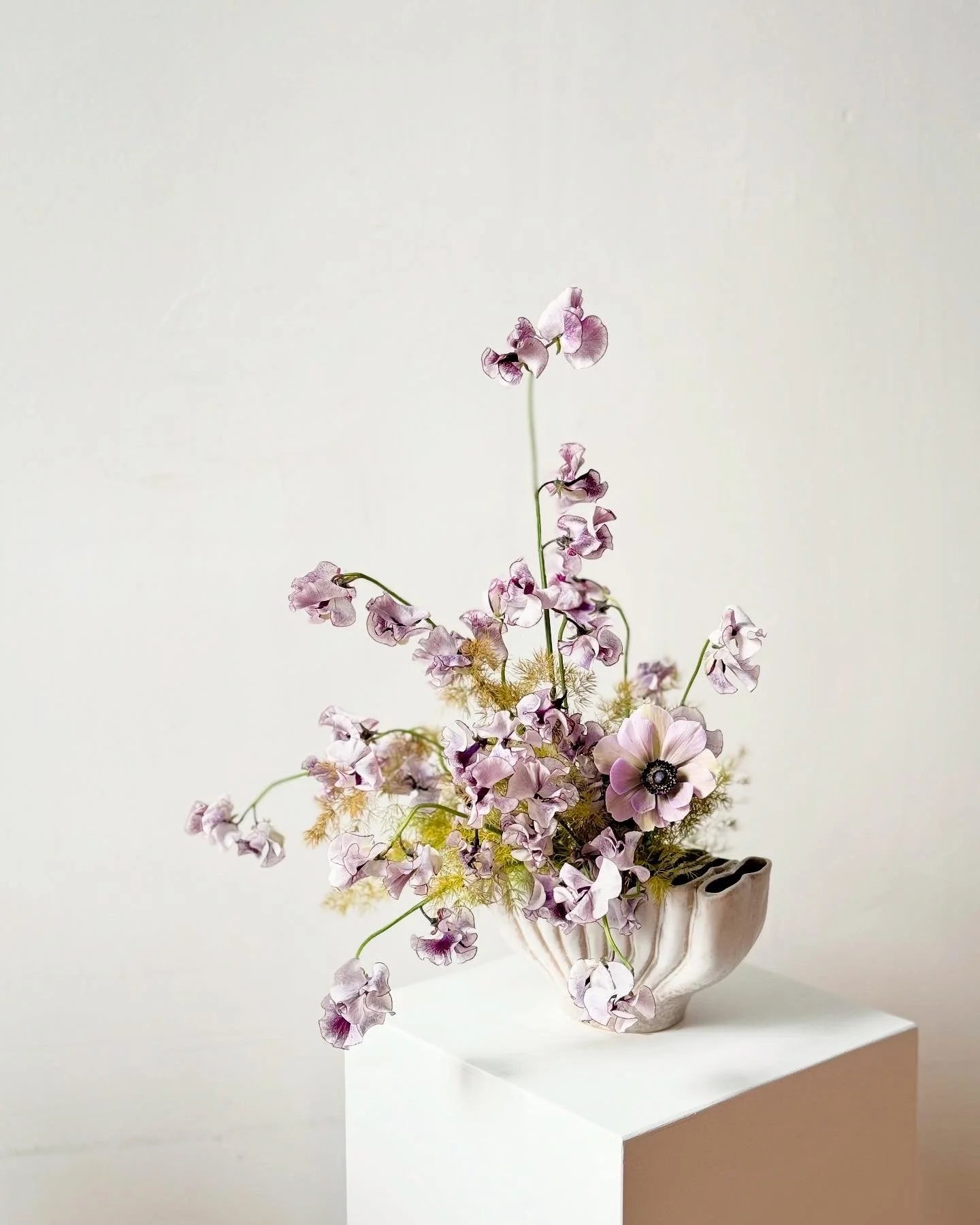 Floral arrangement in a white vase on a light surface with a plain background
