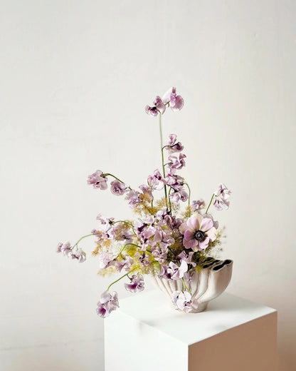 Floral arrangement in a white vase on a light surface with a plain background