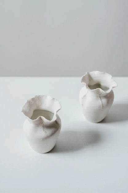 Two white ceramic vases on a light gray surface with a plain background