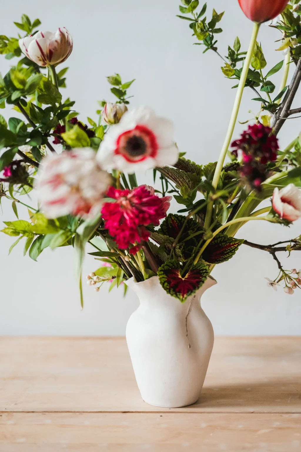 White vase with colorful flowers on a wooden surface