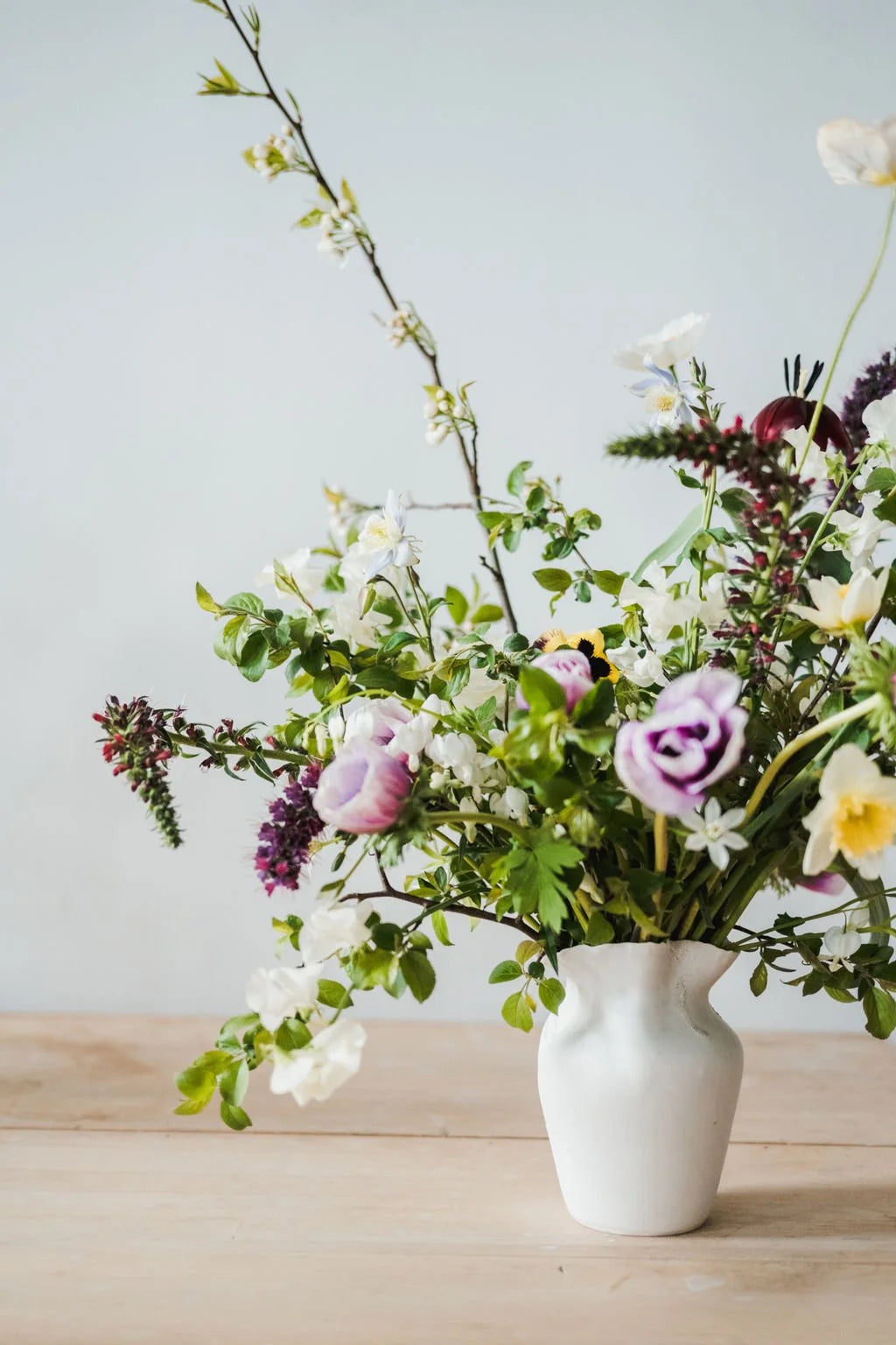 Floral arrangement in a white vase on a wooden surface with a light blue background