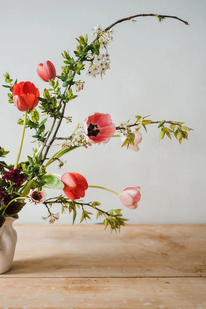 Floral arrangement with red and pink flowers in a vase on a wooden surface.