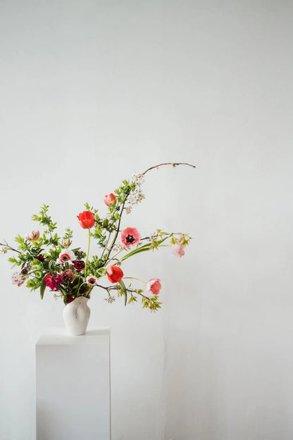 Floral arrangement in a white vase on a white pedestal against a light gray background